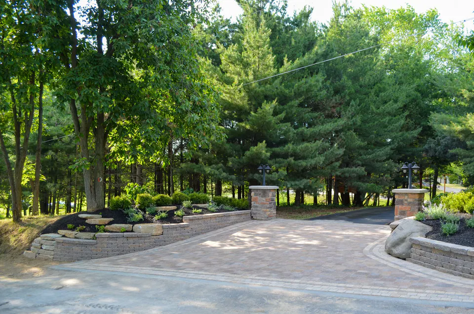 Curved paver driveway through trees with stone piers and planted edges